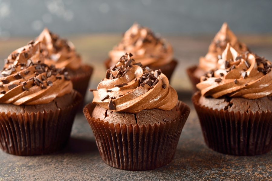 cluster of chocolate cupcakes with chocolate buttercream frosting and chocolate sprinkles and shavings on top with each surrounded by a dark brown cupcake liner