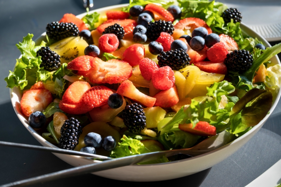 white bowl filled with fruits like blackberry, raspberry, strawberry, blueberries, and kiwis, on top of a bed of lettuce